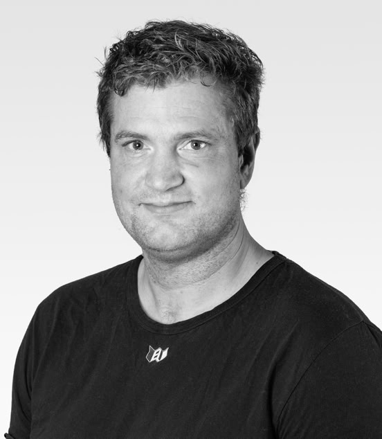 A black and white portrait of a person with short hair, wearing a dark shirt, smiling slightly, against a light gray background.